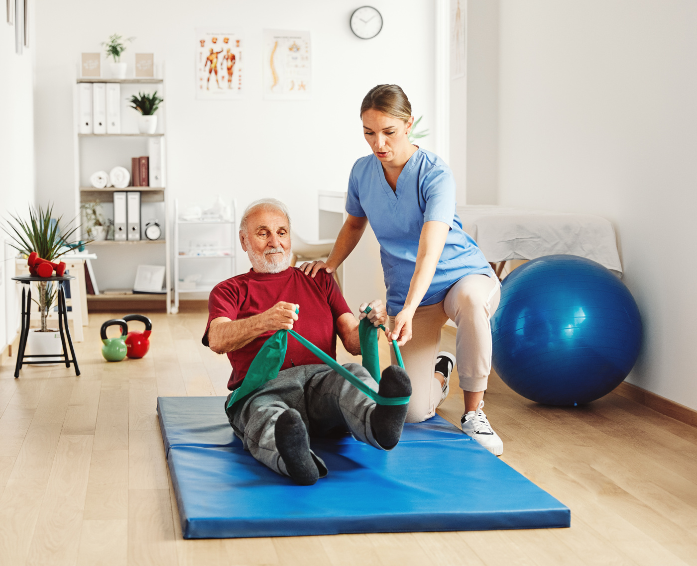 Un fisioterapista FH mostra a un paziente anziano come eseguire correttamente un esercizio con il Theraband.