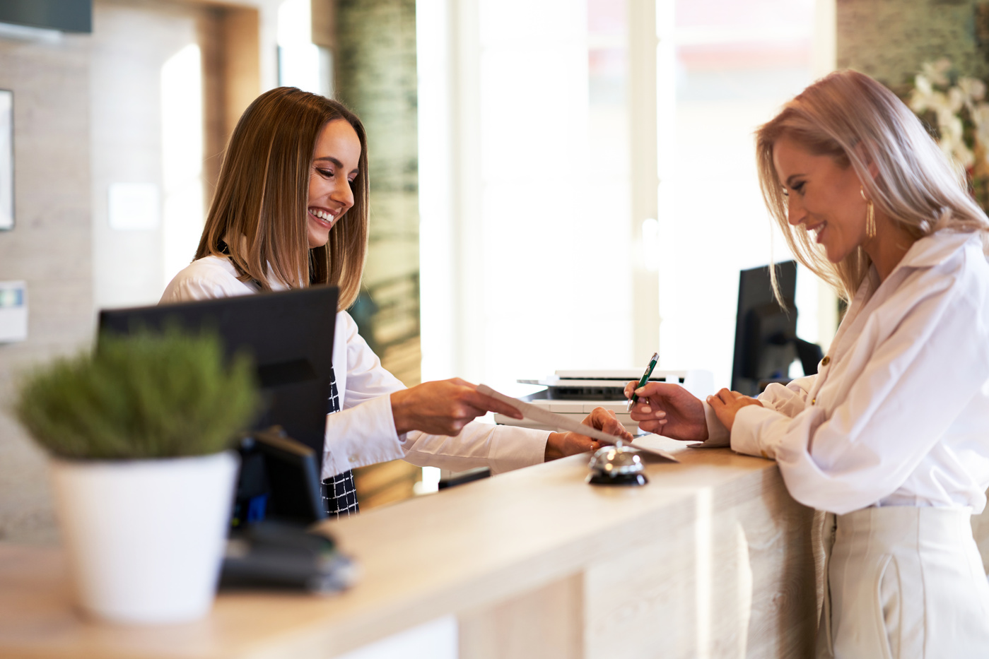 A hotel housekeeping specialist with a federal certificate of competence advises a hotel guest at the front desk of a hotel.