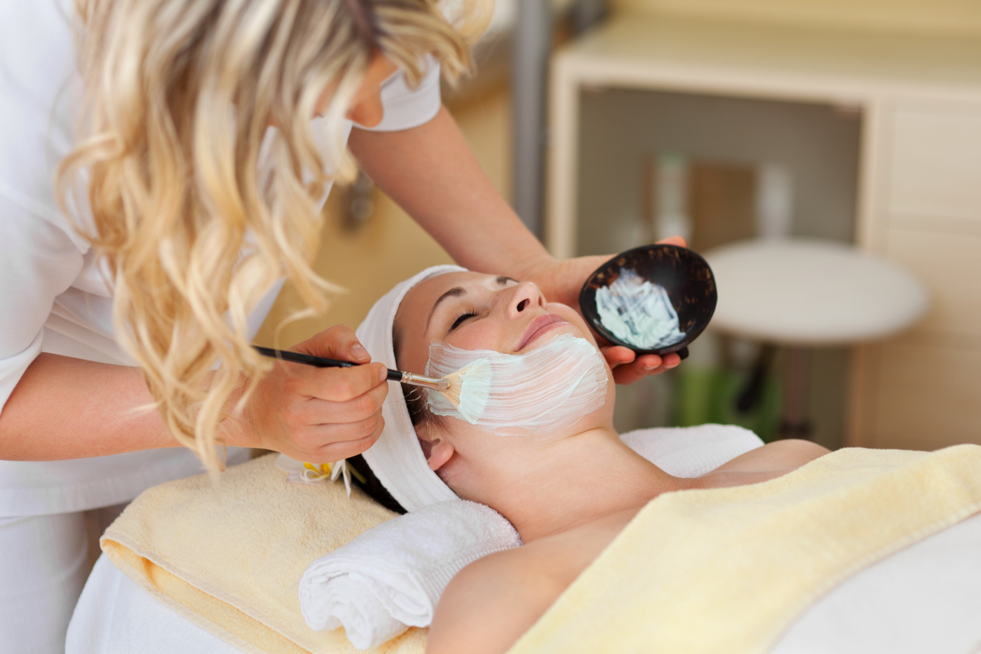 Eine Kosmetikerin verteilt ein wohltuendes Peeling auf die Haut einer Klientin.