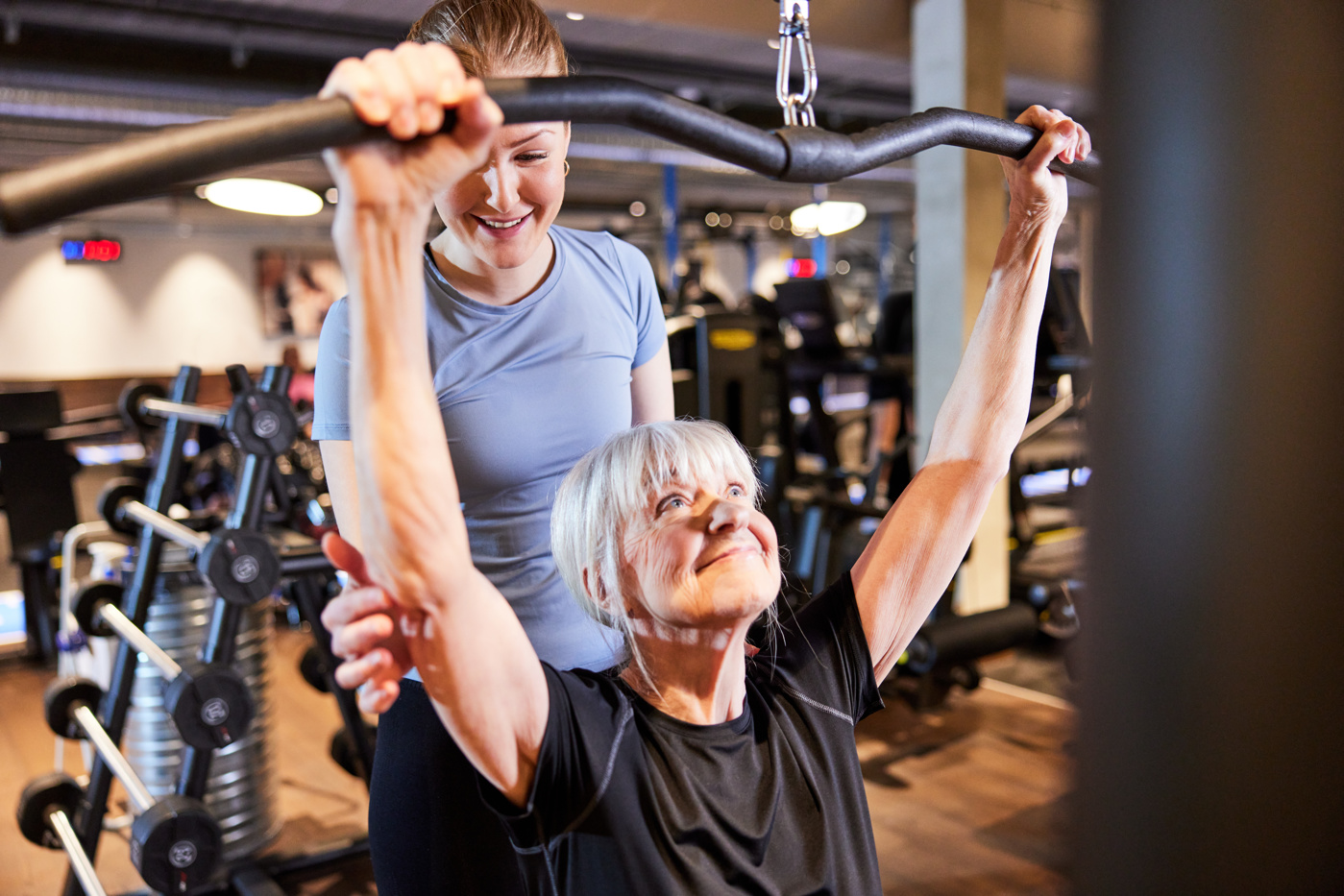 Une spécialiste en promotion de l'activité physique et de la santé avec brevet fédéral guide une cliente dans un centre de fitness pour qu'elle utilise correctement un appareil d'entraînement.