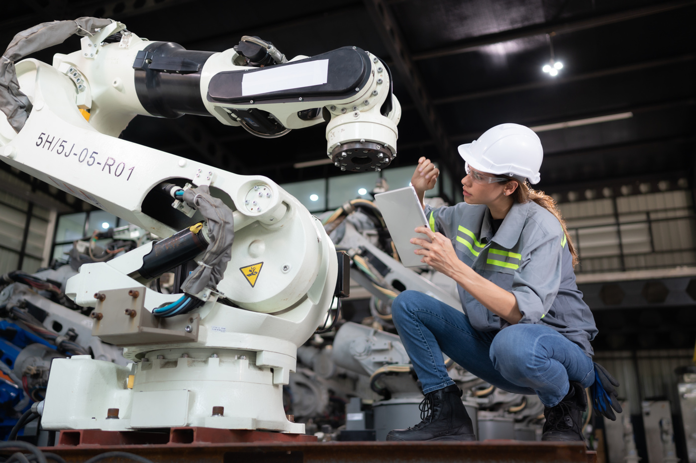 Une technicienne en systèmes, diplômée d'une haute école spécialisée, contrôle un robot de l'industrie.