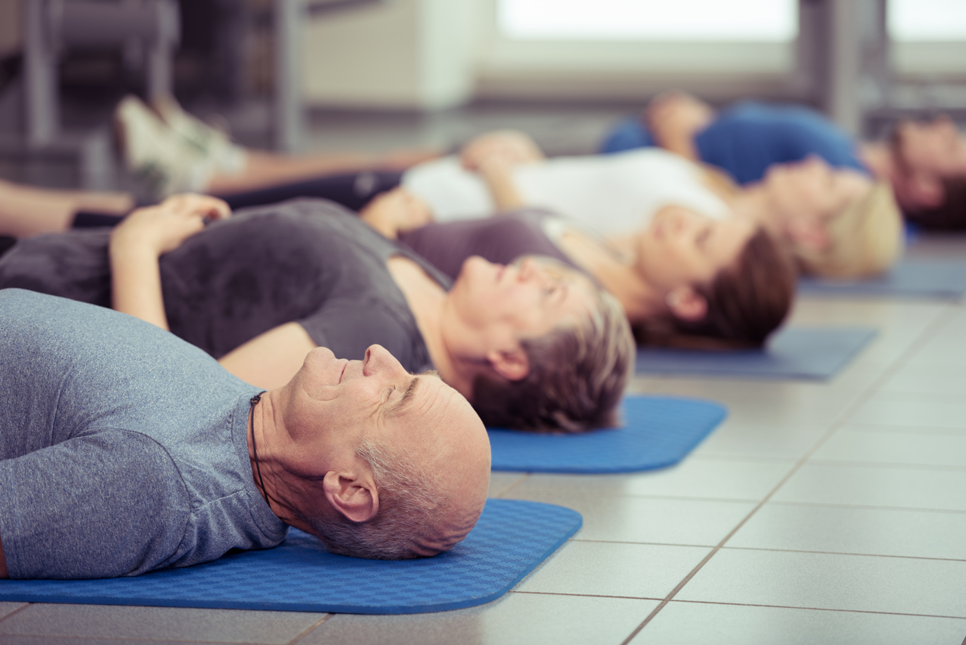 Teilnehmer und Teilnehmerinnen praktizieren nach dem Workout Autogenes Training, um sich zu entspannen.